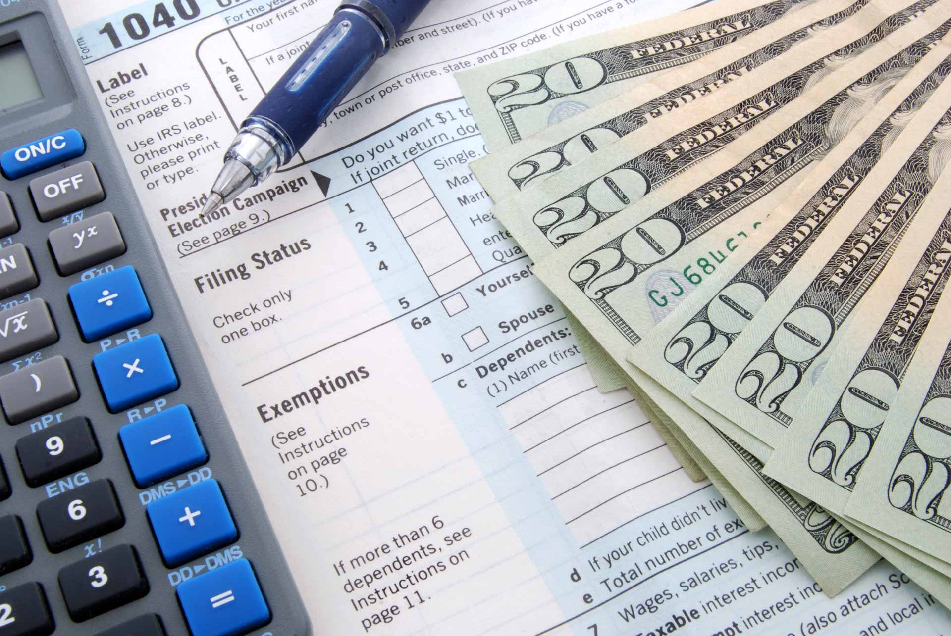 IRS 1040 form on table with pen, calculator, and cash